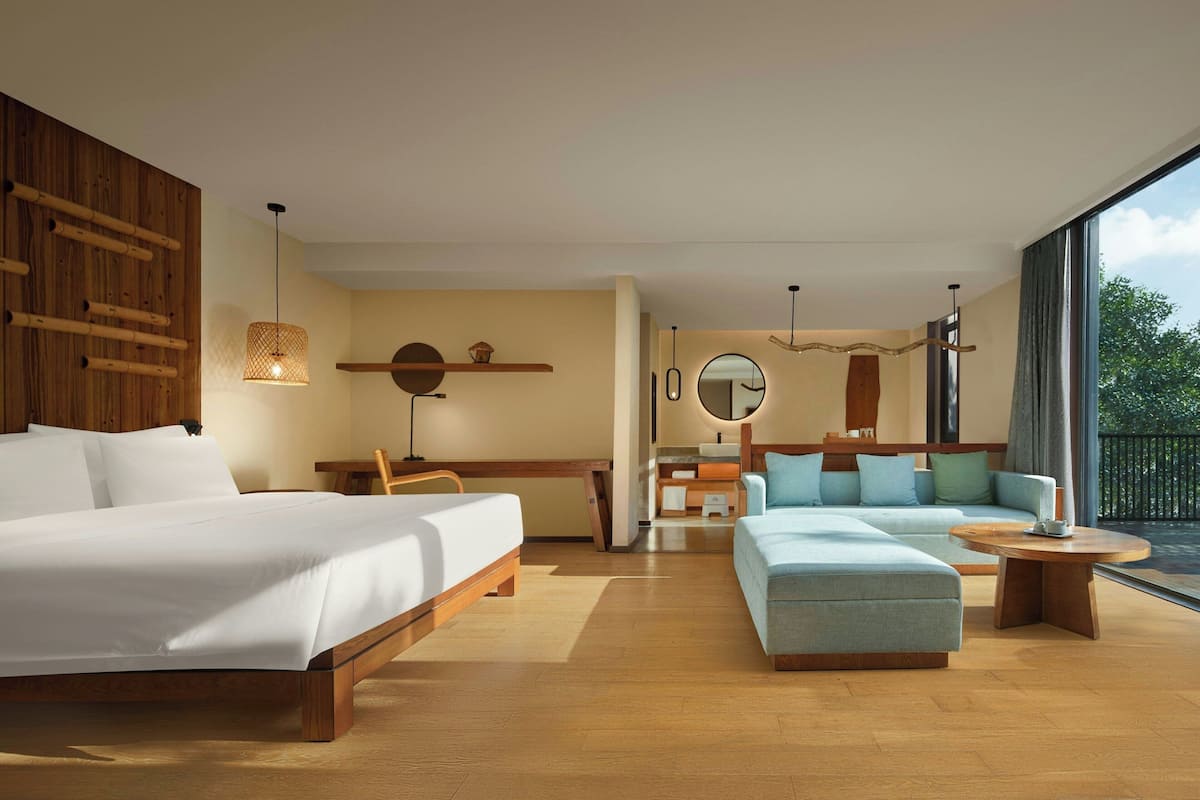 A modern hotel room with a large bed, a sofa, a desk, and a dining area.