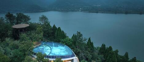 A resort with a circular infinity pool surrounded by lush greenery and mountains in the background.