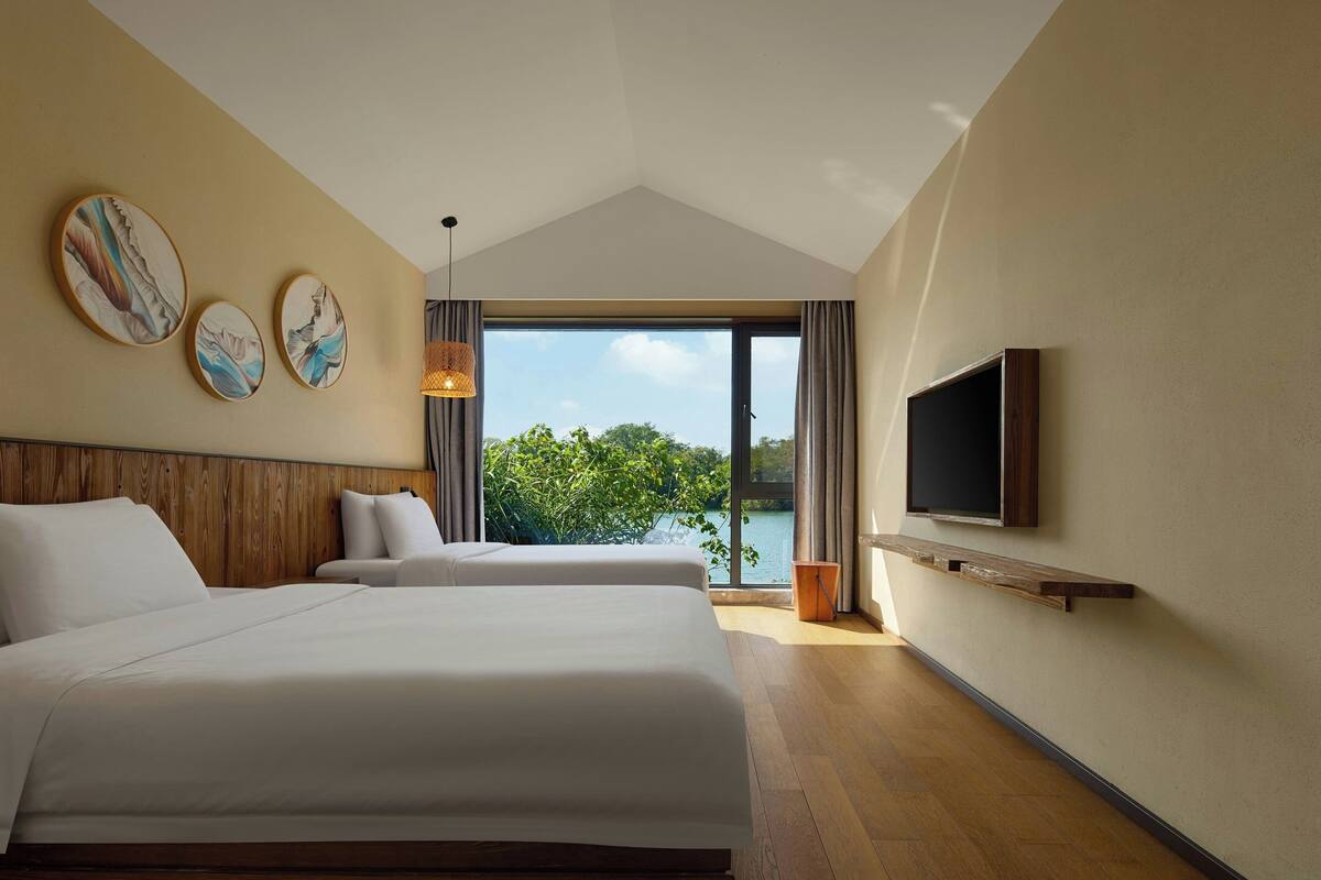 A hotel room with two beds, a TV, and a view of a lake.