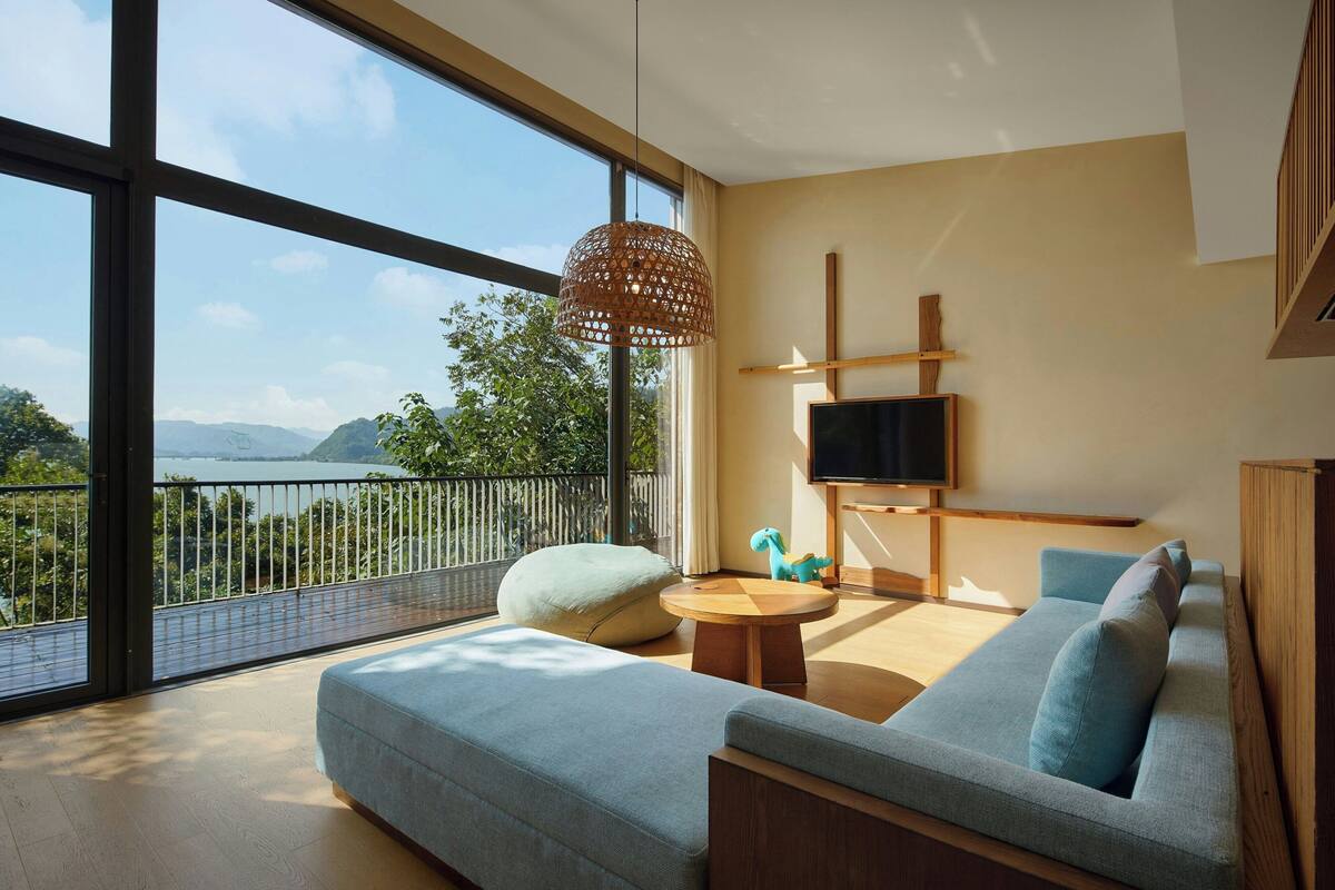 A modern living room with a large window, a sofa, a coffee table, and a TV.