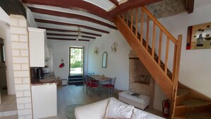 Ein gemütliches Wohnzimmer mit einem weißen Sofa, roten Kissen, einer Holztreppe und einer Küche im Hintergrund.