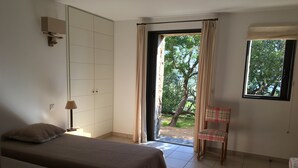 A room with two beds, a chair, a lamp, a wardrobe, and a window with a view of trees. - 5 bedroom house in Palombaggia (Porto Vecchio) with view and direct access to the sea (Porto-Vecchio)