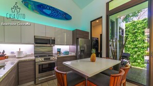 A modern kitchen with stainless steel appliances, a dining area with wooden chairs, and a large fish mural on the ceiling. - Surf In Surf Out Casa Otto Beachside Colorada (Puntarenas Province)