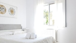 Un dormitorio luminoso con una cama grande, un radiador y una ventana con vistas a zonas verdes.