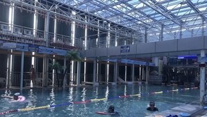 En indendørs swimmingpool med tydelige baner, et springbræt og et tag af glas.