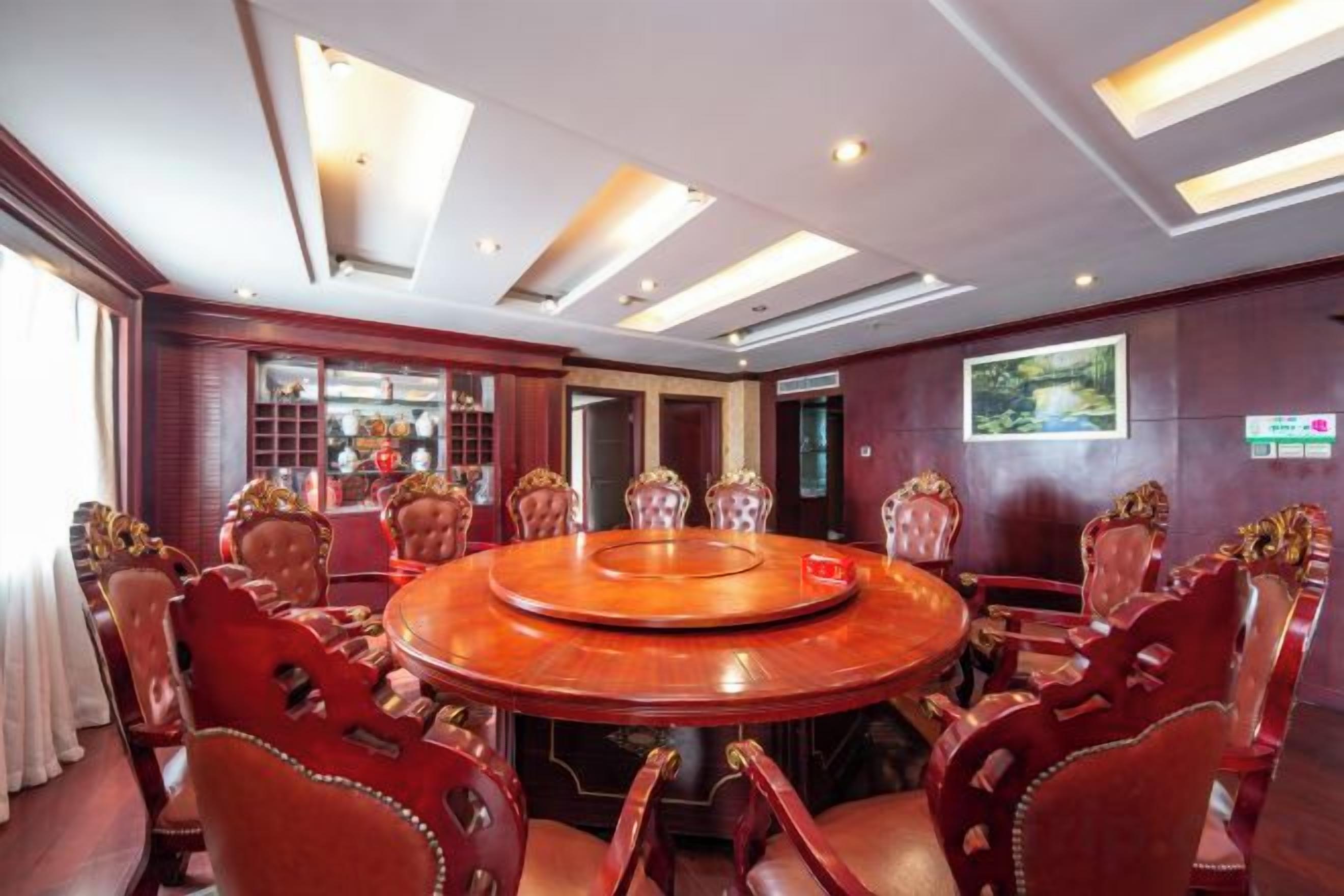 A conference room with a round table, red upholstered chairs, and a large window.