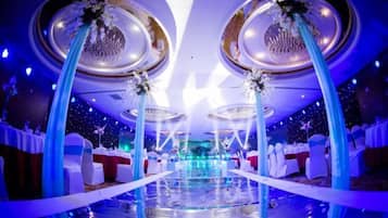 A hotel ballroom with a reflective floor, round tables, and blue drapes.