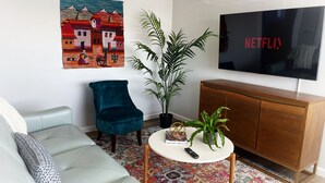 Un salon comprenant un canapé, un fauteuil turquoise, une table basse avec une plante, un téléviseur et un tapis coloré.