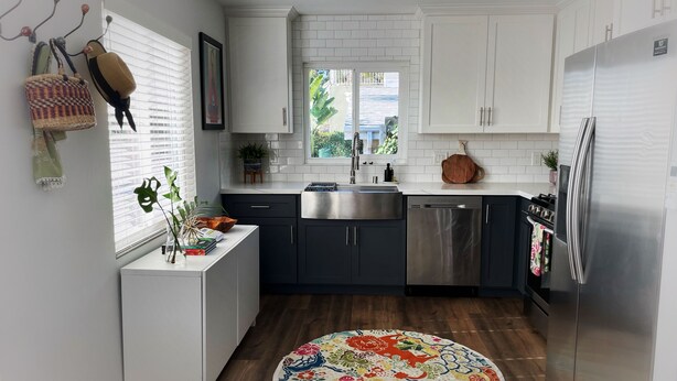 Une cuisine moderne avec des meubles blancs, des appareils en acier inoxydable et un tapis aux couleurs vives.