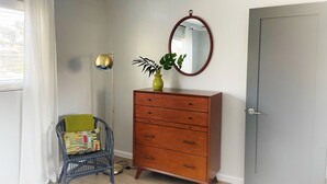 Une pièce comprenant une commode en bois, un miroir, une chaise et une fenêtre avec des rideaux.