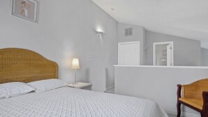 Une chambre à coucher comprenant un lit, une table de chevet, une lampe, une chaise, une armoire et un tableau encadré accroché au mur.