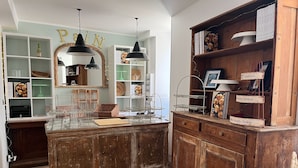 A bakery with a rustic wooden counter, shelves with baked goods, and hanging black pendant lights. - Le Fournil de Flavigny The Bakery rooms (Flavigny-sur-Ozerain)