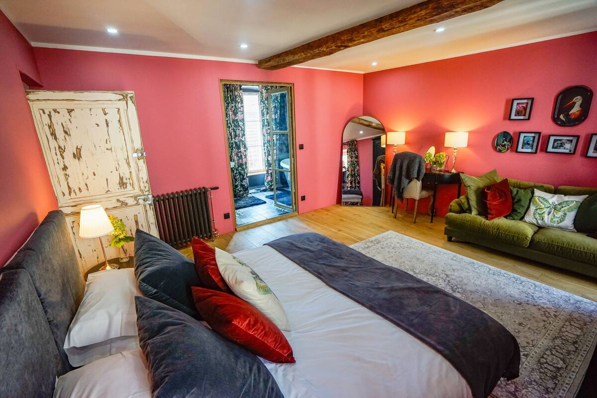 Quarto com uma cama grande, um sofá verde e teto de madeira.