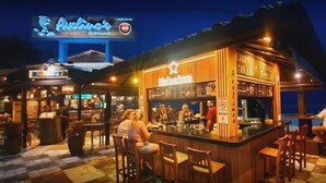 A bar area with wooden bar counters and stools, a sign for 'Avelinair Restaurant', and a Heineken logo. - Oceanview Apartment in Guarujá: Fast WiFi & Smart TV (Guarujá - SP)