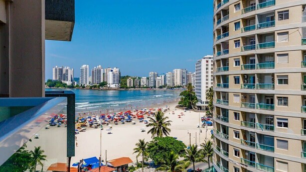 A beach view from a high-rise building with multiple balconies, a sandy beach, and a city skyline in the background. - Oceanview Apartment in Guarujá: Fast WiFi & Smart TV (Guarujá - SP)