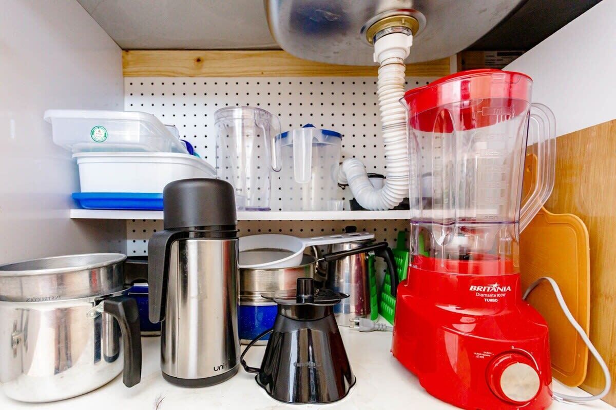 Eine Küche mit verschiedenen Geräten und Behältern, darunter ein roter Mixer, Edelstahl-Töpfe und Plastikboxen.