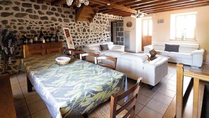 Una habitación rústica con paredes de piedra, techo de madera, una mesa de comedor con mantel estampado y un conjunto de sofás.