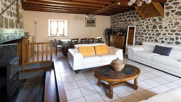 Amplia sala de estar con chimenea, sofás blancos, una mesa redonda y una pared de piedra.