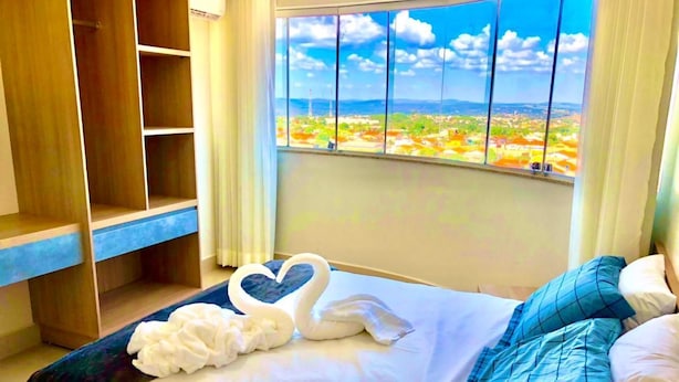 Ett hotellrum med en säng, en garderob i trä och ett stort fönster med utsikt över stadsbilden.