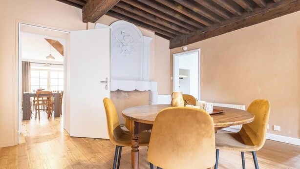 Un coin repas avec une table en bois et des chaises jaunes, une porte blanche ornée d’un panneau décoratif et un plafond en bois.