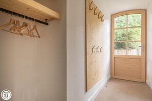 Una habitación con puerta de madera, ventana con vista a follaje y estante de madera con perchas.