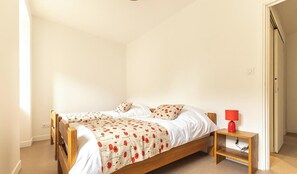 Un dormitorio con una cama doble, una mesita de noche con lámpara y una puerta que da a otra habitación.