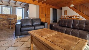 A spacious living area with a wooden ceiling, a leather sofa, a wooden coffee table, and a kitchen area in the background. - Le Balladou - Vernines (VERNINES)