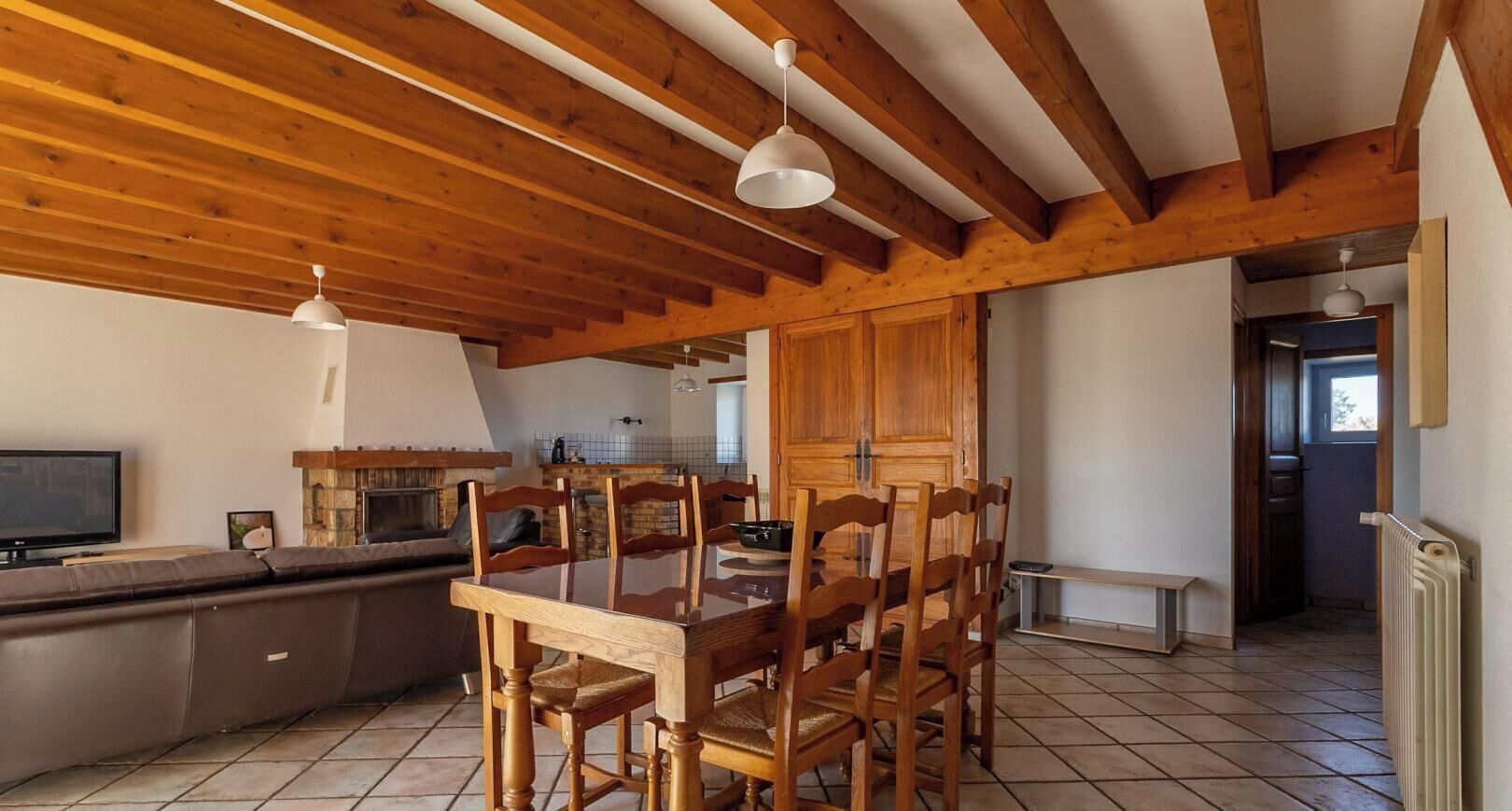 A dining area with a wooden table and chairs, a TV, and a stone fireplace.