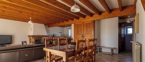 A dining area with a wooden table and chairs, a TV, and a stone fireplace.
