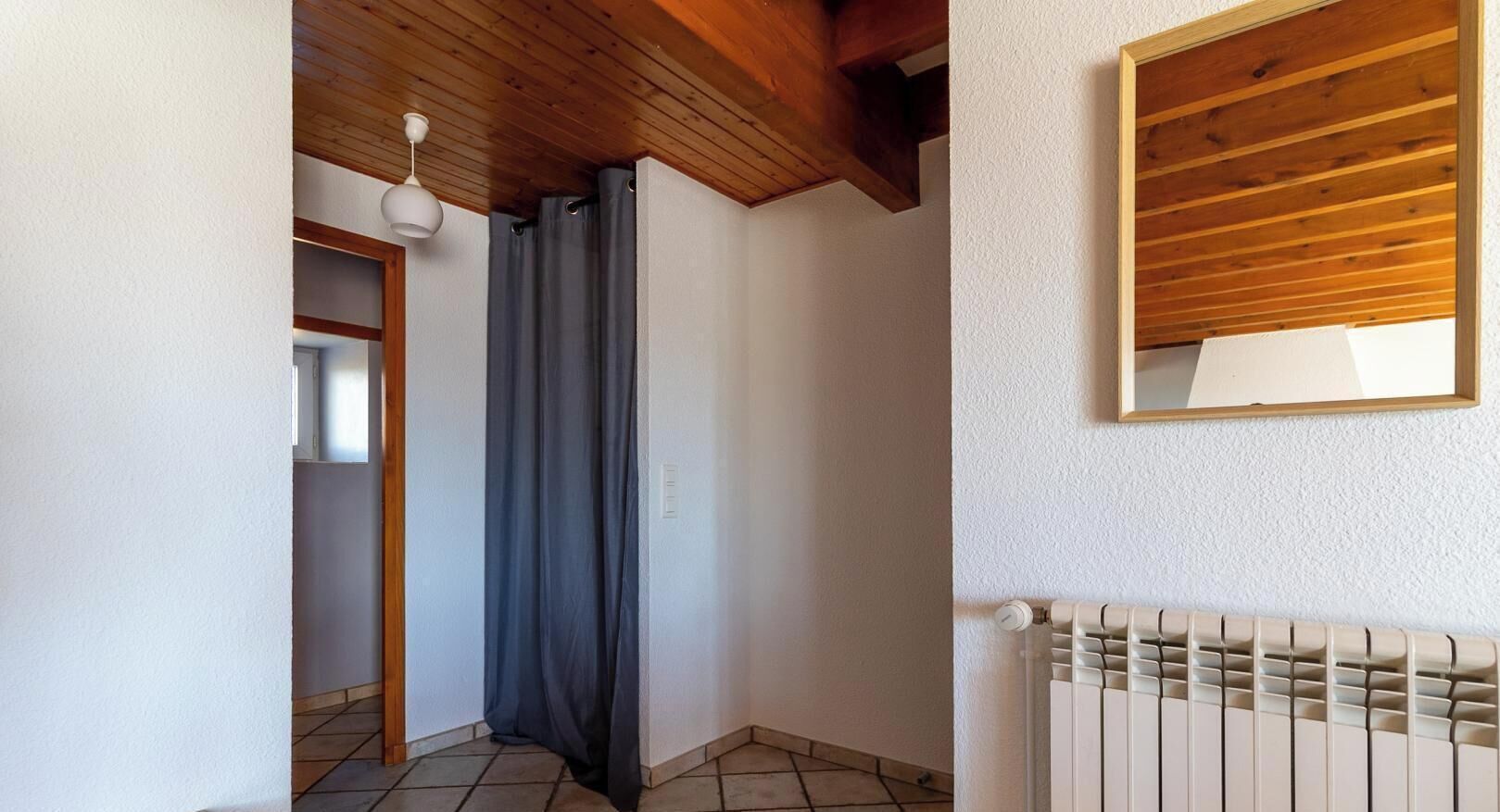 Un estrecho pasillo con techo de madera, un radiador y una ventana con marco de madera.