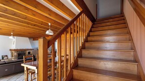 A wooden staircase with a railing, leading to a room with a fireplace and a dining area. - Le Balladou - Vernines (VERNINES)