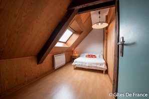 Cozy attic bedroom with a sloped ceiling, wooden paneling, and a skylight. Features a single bed, bedside table, and radiator.