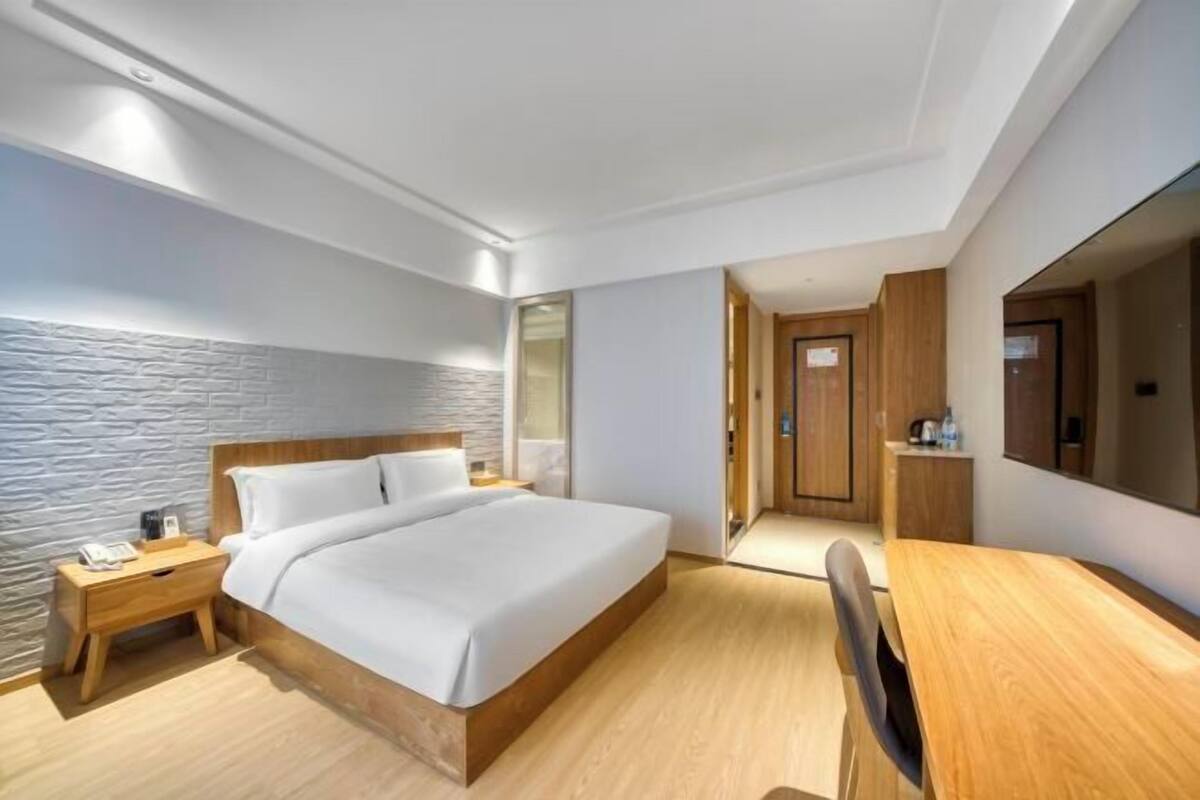 Ein modernes Hotelzimmer mit einem großen Bett, einem Holfnachtkästchen und einem Schreibtisch mit Stuhl.