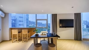 A modern hotel room with a large window, a flat-screen TV mounted on the wall, a dining table with chairs, and a small plant on the table. - Hotel Jagri Taizhou (Taizhou)