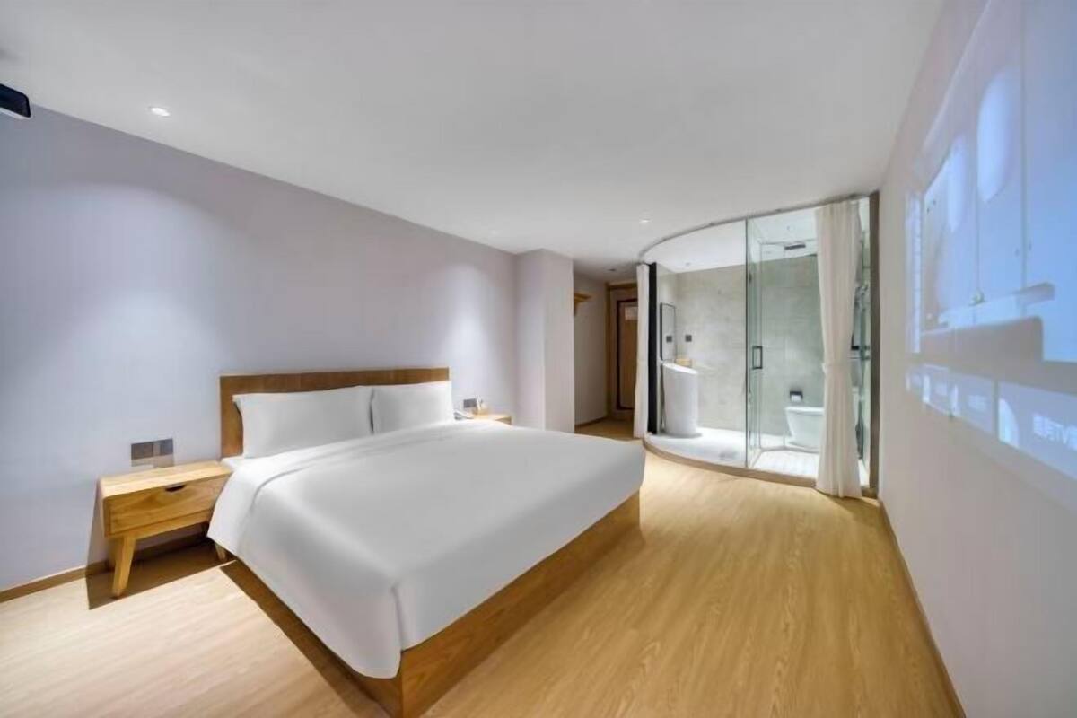 Ein modernes Hotelzimmer mit einem hölzernen Bett, einem Nachttisch, einer Glasdusche und Blick auf die Stadt.
