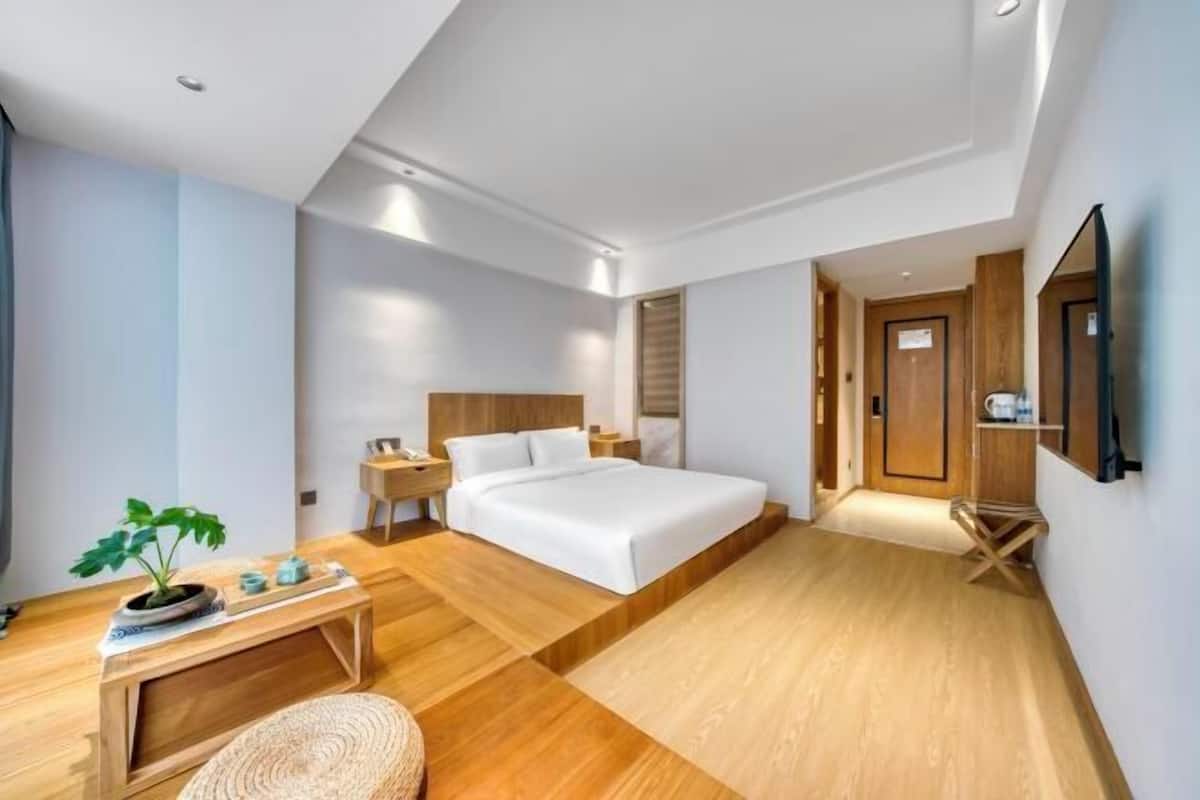 Ein modernes Hotelzimmer mit einem großen Bett, Holzboden, einem kleinen Schreibtisch, einem Nachttisch und einer Topfpflanze.