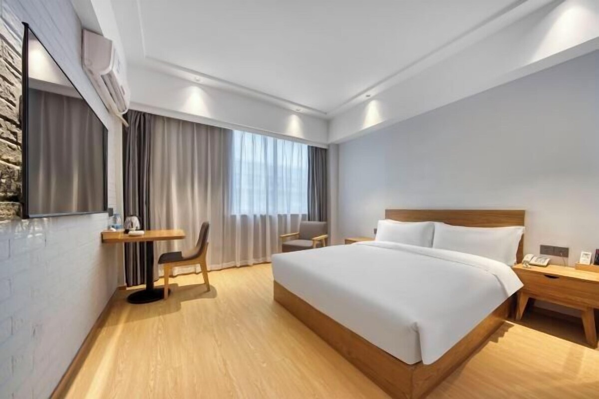 A hotel room with a large bed, a desk, a chair, a TV, and a window with curtains.