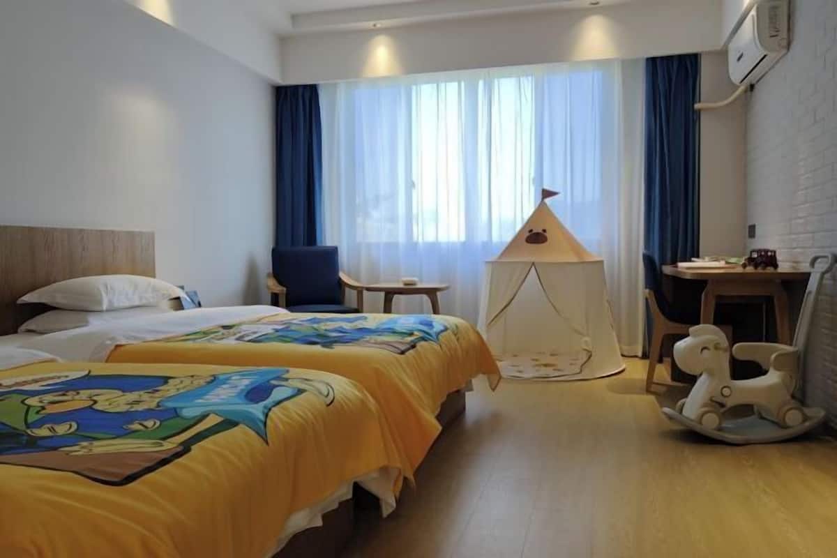 Ein Hotelzimmer mit zwei Betten, einem kleinen Tisch, einem Stuhl, einer Lampe und einem Schaukelpferd.
