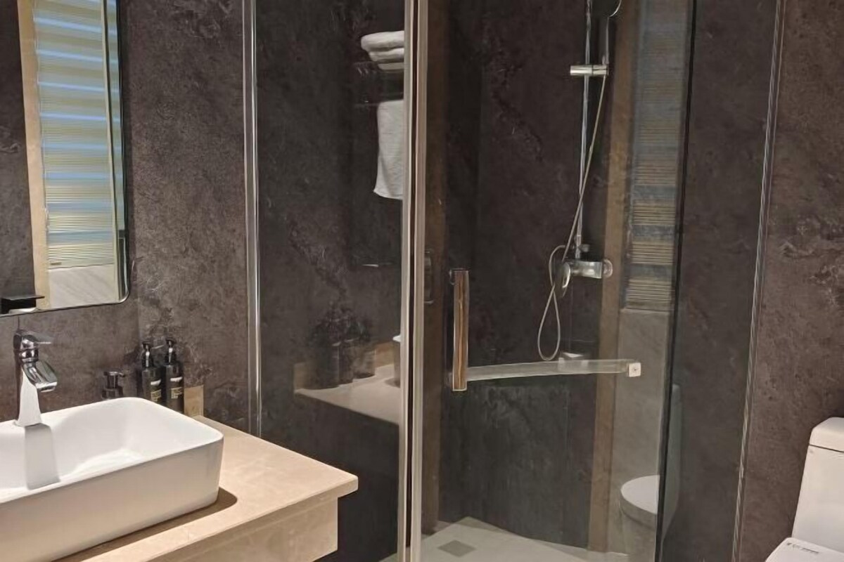 A modern bathroom with a glass-enclosed shower, a white sink, and a large mirror.