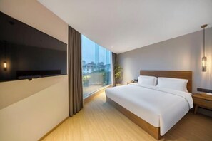 Een moderne hotelkamer met een groot bed, een aan de muur bevestigde televisie, een nachtkastje en uitzicht op de stad door een groot raam.