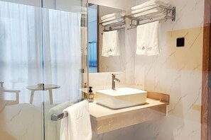 Een moderne badkamer met een douchecabine van glas, een witte wastafel en een handdoekrek met meerdere handdoeken.