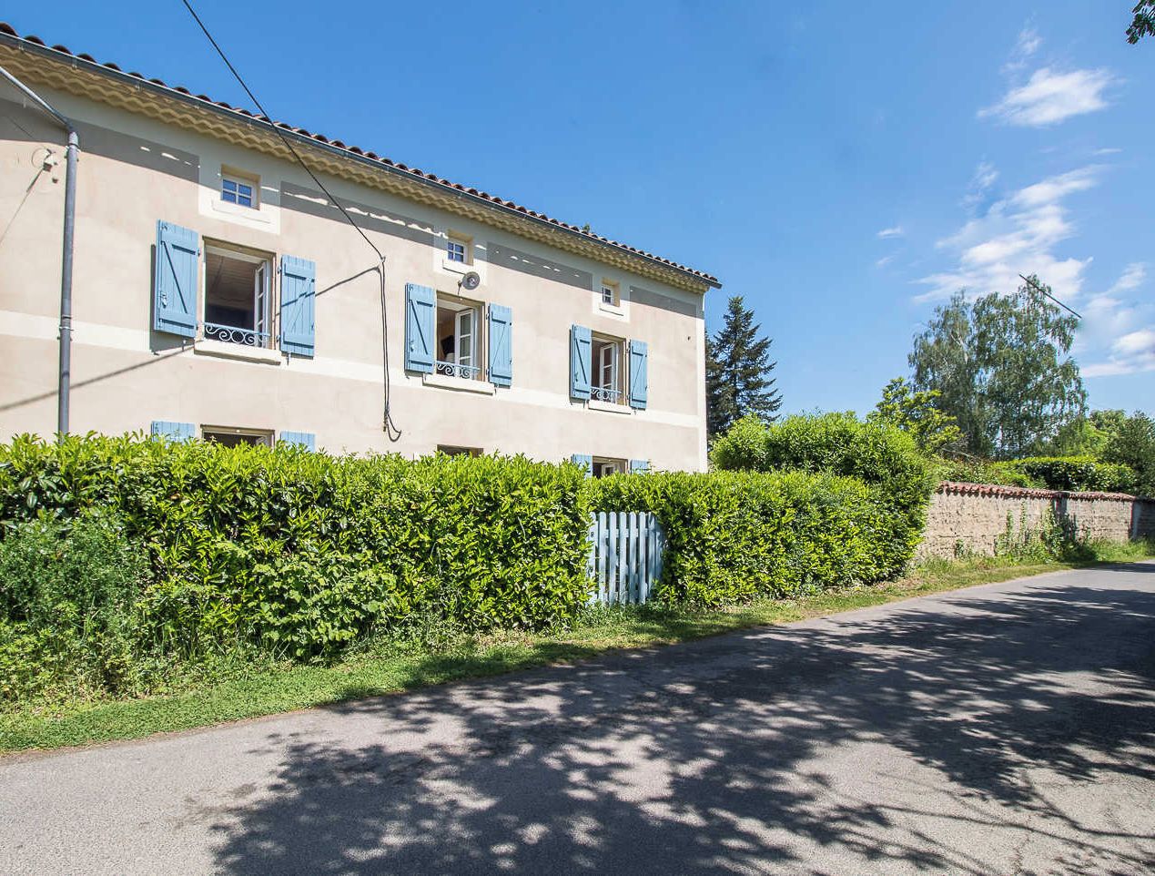 Un bâtiment à deux étages, doté d’une façade beige, de volets bleus et d’une allée pavée.