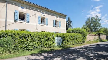 Un bâtiment à deux étages, doté d’une façade beige, de volets bleus et d’une allée pavée.