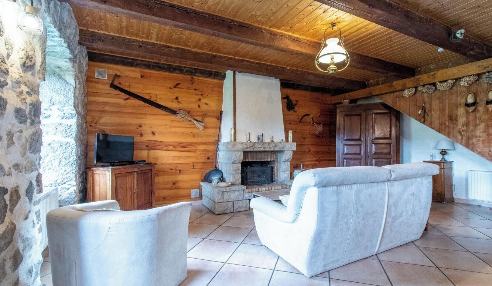 A log cabin interior with a stone fireplace, wooden walls, a television, and a stone wall on the left.