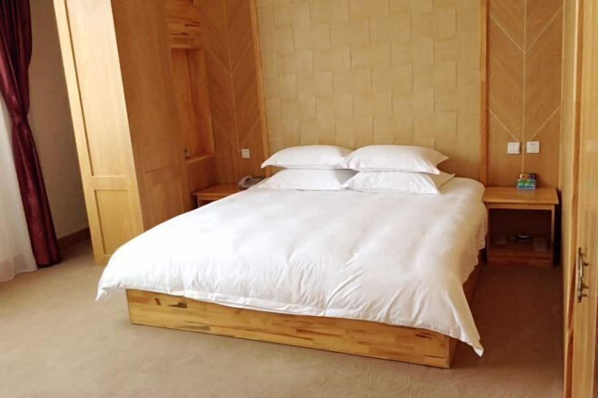 A wooden bed with white bedding in a room with wooden walls and a carpeted floor.