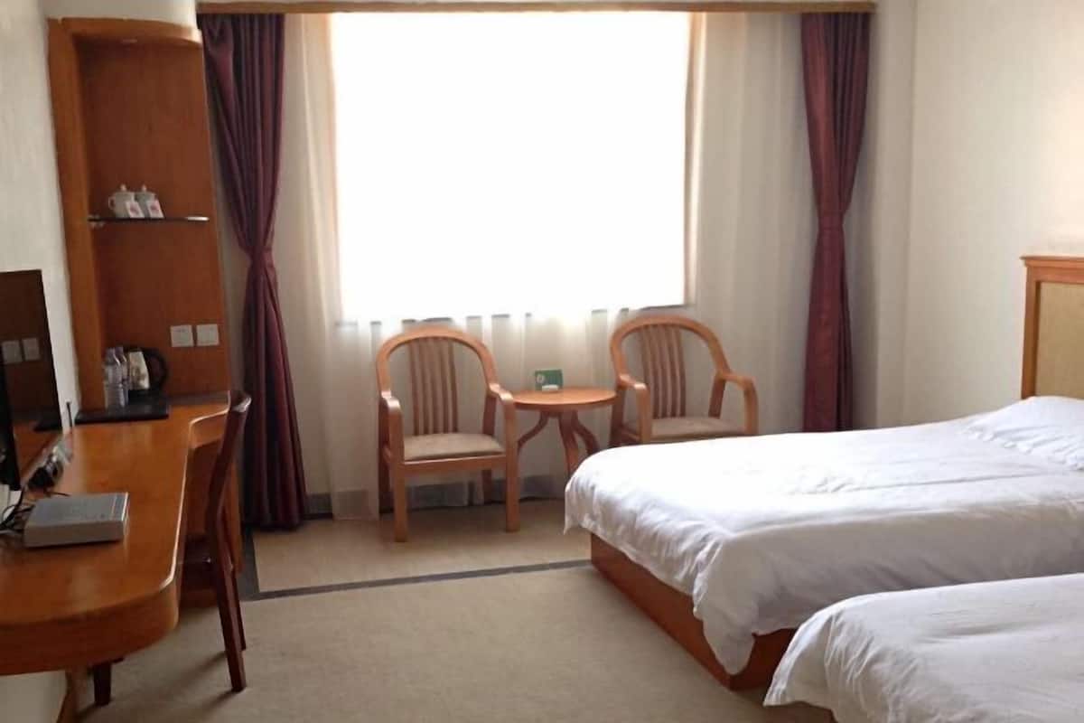 A hotel room with a bed, two chairs, a small table, a wooden cabinet, and a window with curtains.