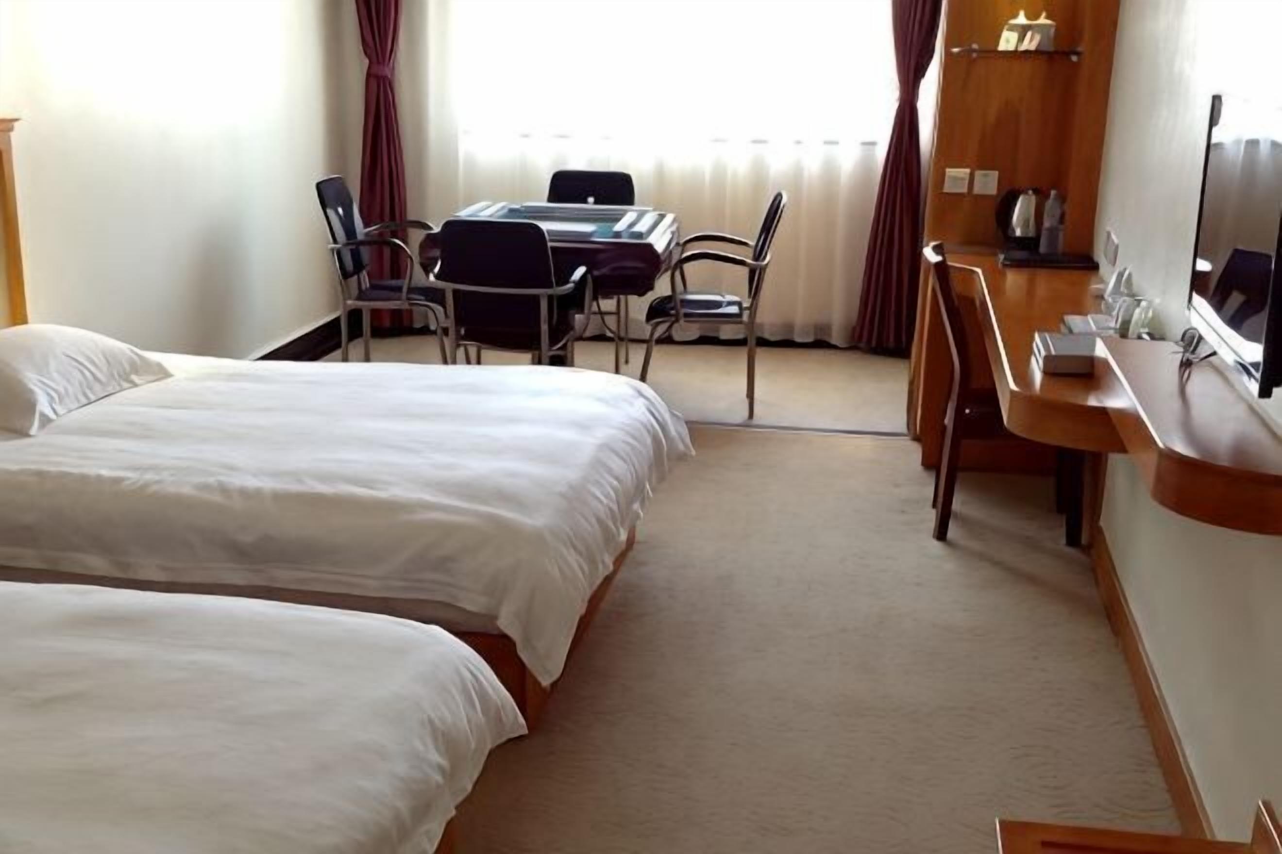 Une chambre d’hôtel avec deux lits, un bureau, une chaise, une télévision et une fenêtre avec des rideaux.