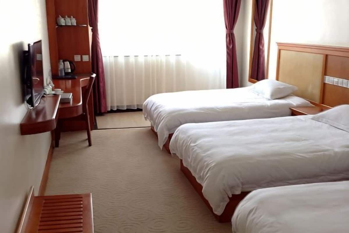 A hotel room with two beds, a desk, a chair, a TV, and a window with curtains.