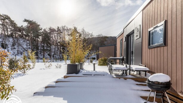 Ein modernes Gebäude mit Holzfassade, einer überdachten Außenbestuhlung und einer verschneiten Landschaft.