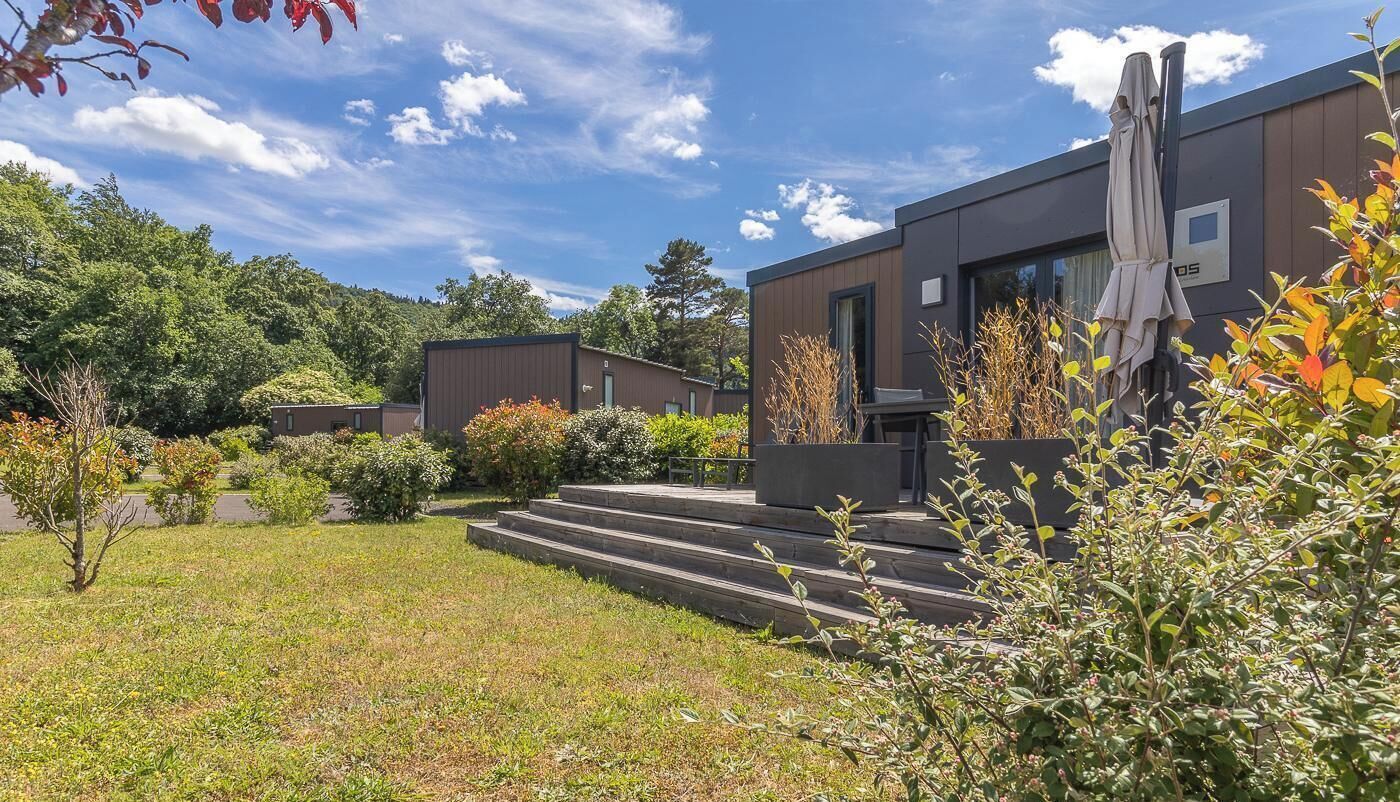 A modern building with a flat roof, a covered outdoor seating area, and a well-maintained garden with steps leading to the entrance.